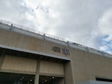 A large building facade with a beige tiled exterior is visible, featuring a colorful geometric star design and text in multiple languages.