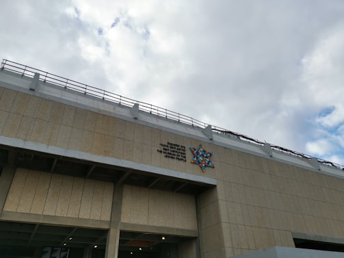 A large building facade with a beige tiled exterior is visible, featuring a colorful geometric star design and text in multiple languages.