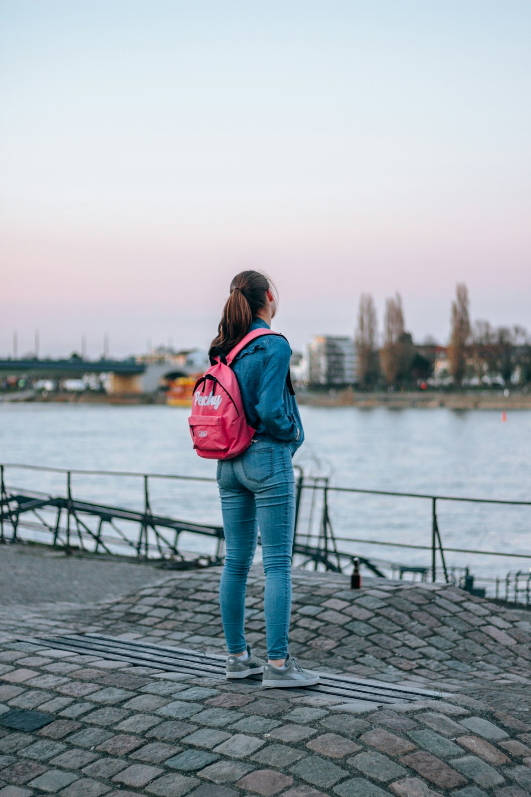 woman wearing pink backpack standing beside body of water during daytime