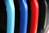 A close-up view of several colorful plastic hangers arranged in a row. The hangers are primarily in shades of blue, red, and black, with a soft-focus background.