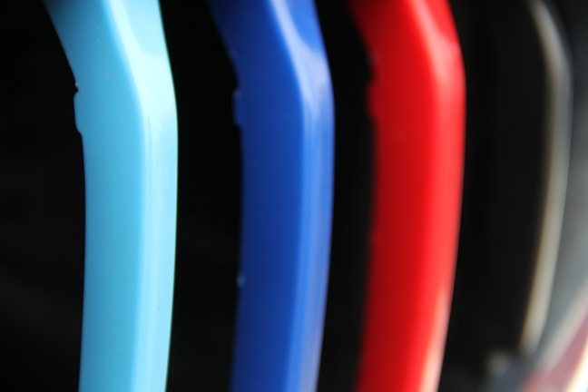 A close-up view of several colorful plastic hangers arranged in a row. The hangers are primarily in shades of blue, red, and black, with a soft-focus background.