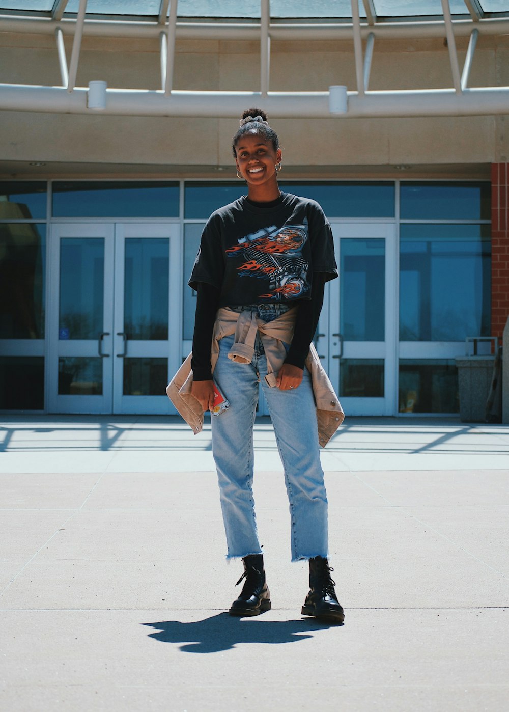 woman in black crew-neck shirt, blue denim jeans and black leather shoes standing near white painted building