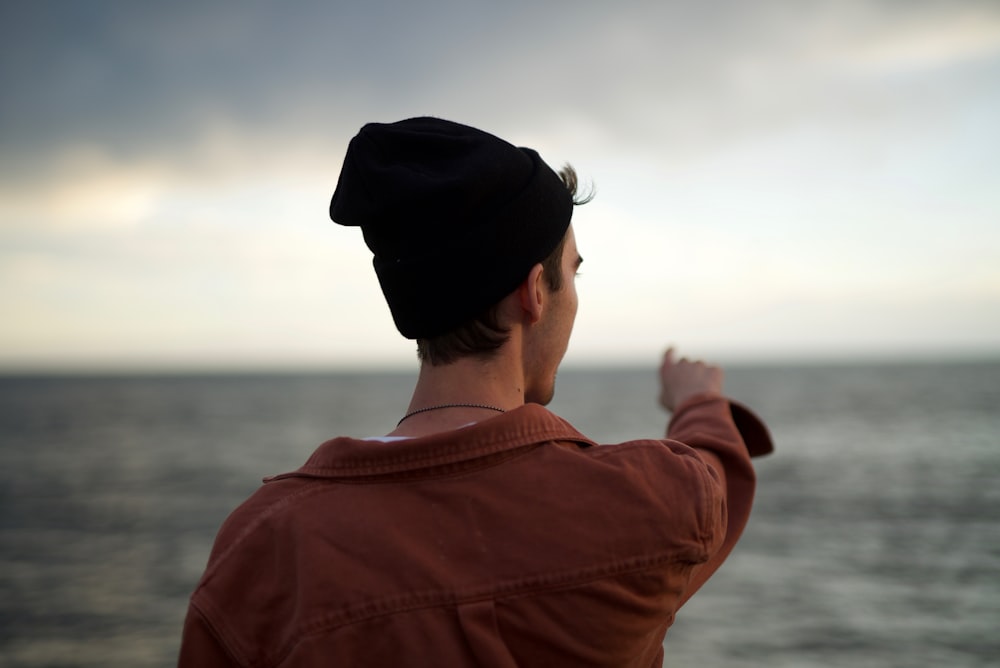 man wearing red jacket standing and pointing on sea