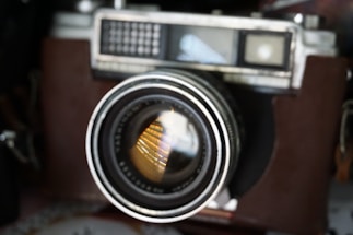 Black and white close-up of a vintage film camera lens reflecting soft light.