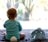 A baby wearing light blue pajamas with a fluffy white tail sits on a soft carpet facing a large window. The baby's head is adorned with soft bunny ears. Beside the baby sits a plush blue bunny toy, mirroring the baby's attire and ears.