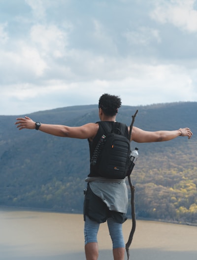 person standing on cliff under white clouds