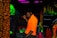 A person wearing a bright orange shirt holds a golf club in a dark, neon-lit environment that resembles a cosmic or underworld-themed setting. The background features vibrant colors and abstract patterns, with elements resembling glowing stones and caverns.