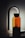 A sleek, modern glass water bottle with black lettering stands upright against a softly lit background. The bottle has a distinctive, elegant spout attachment, resembling a sophisticated dispenser or faucet, casting a gentle shadow.