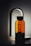 A sleek, modern glass water bottle with black lettering stands upright against a softly lit background. The bottle has a distinctive, elegant spout attachment, resembling a sophisticated dispenser or faucet, casting a gentle shadow.
