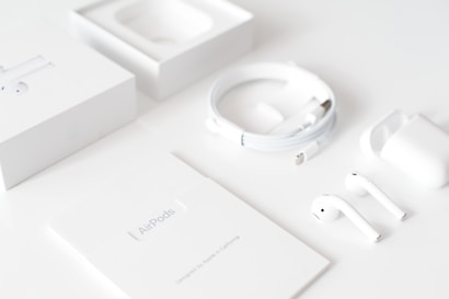 A neatly arranged layout of a tech product setup featuring wireless earbuds. The components are spread across a white surface, including two earbuds, a charging case, a charging cable, and accompanying packaging materials. The overall aesthetic is minimalist with a sleek and clean design.