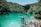A scenic view of a turquoise lagoon surrounded by lush green forested hills. People are engaging in leisure activities such as swimming, paddling in small boats, and preparing to jump from a wooden platform. The atmosphere is lively and adventurous, with a group of people gathered near the jumping platform, capturing the vibrant outdoor spirit.