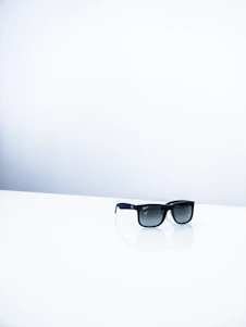 Close-up of a sleek black and gold sunglasses resting on a minimalist white surface.