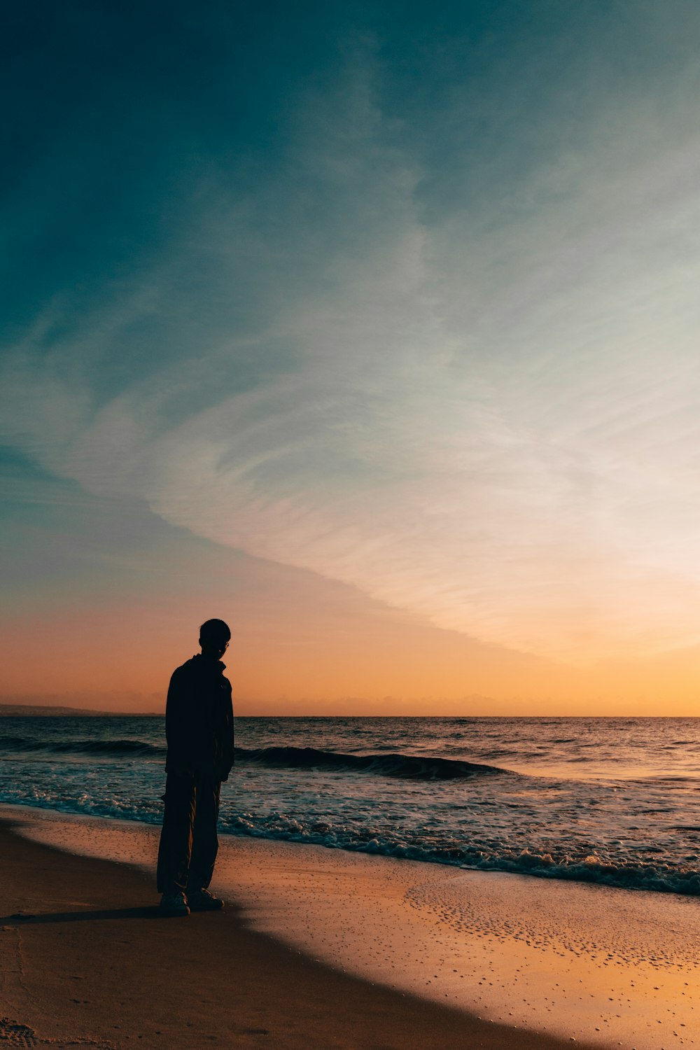silhouette person standing beside seashore during sunset