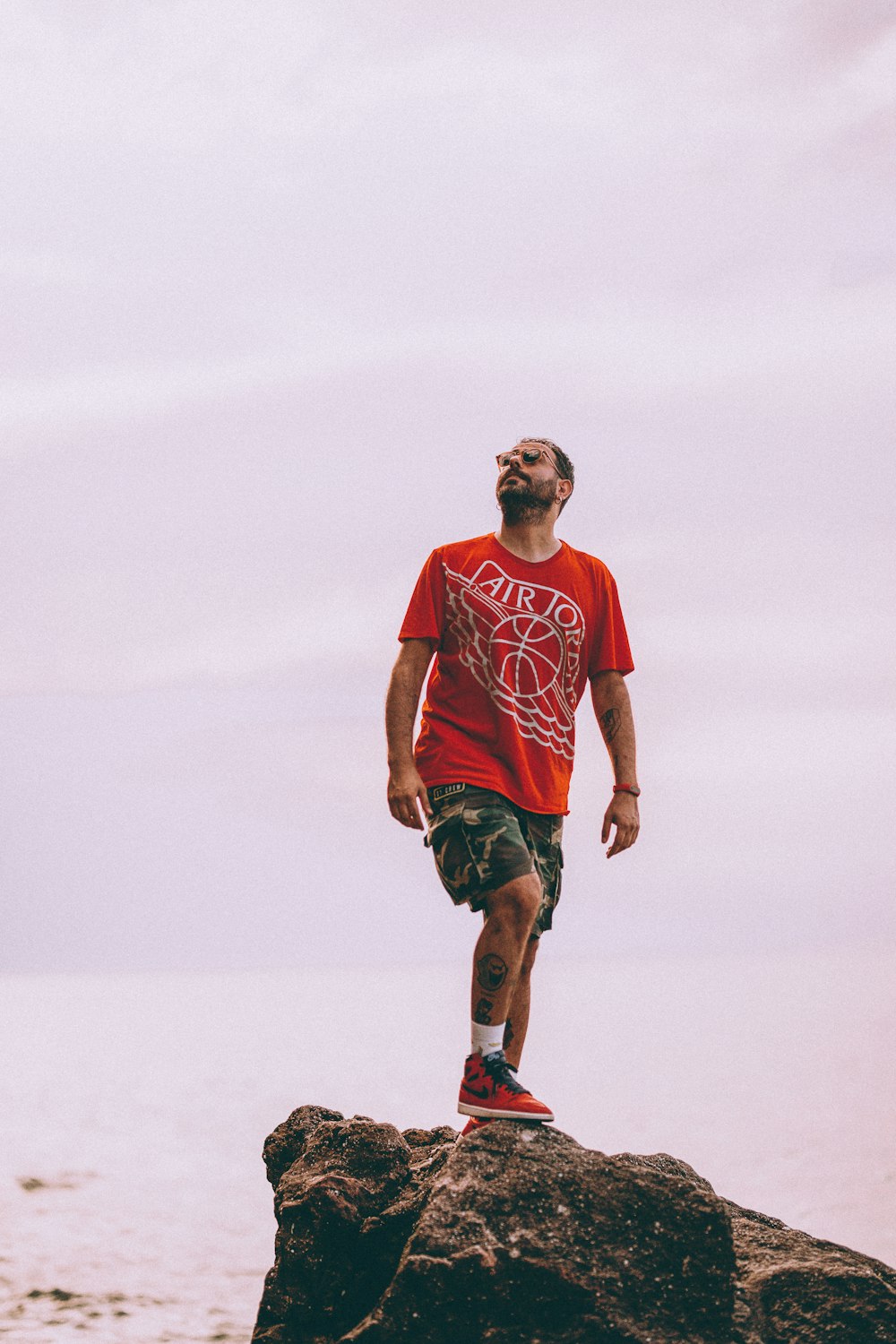 Foto hombre vestido con una camiseta roja de Air Jordan parado en la cima  de una roca marrón – Imagen Marrón gratis en Unsplash