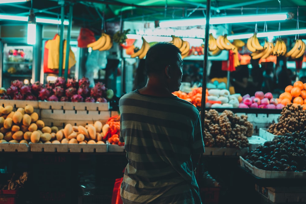 man standing beside fruits in market during night time