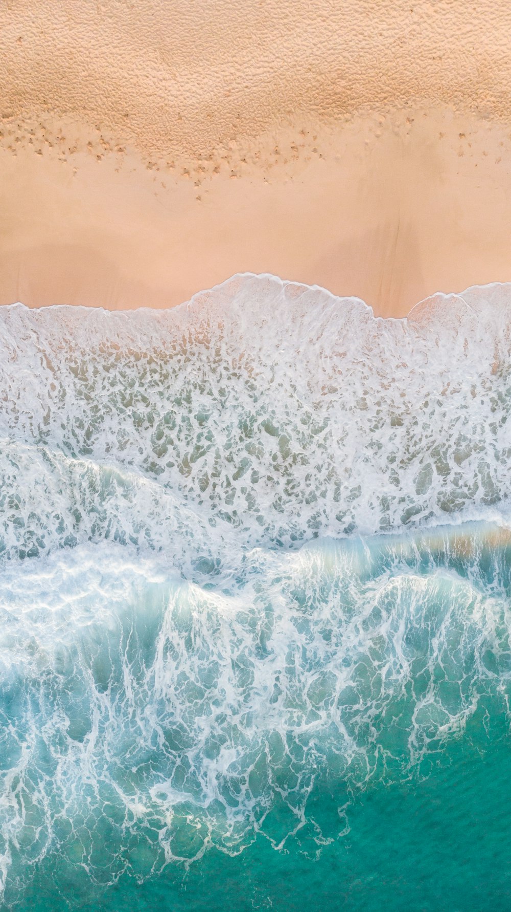 Luftaufnahmen von Wellen, die am weißen Sandstrand plätschern