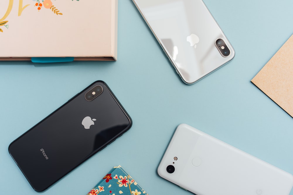 Three different models of referbished Apple iPhones on a blue table with a notebook and a letter.