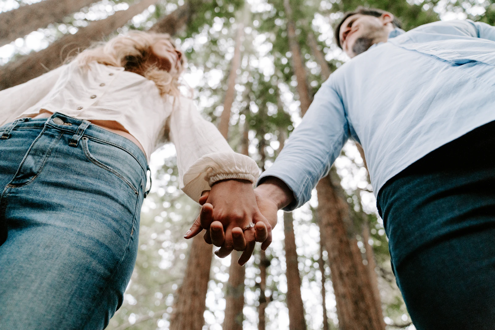 A couple holding hands viewed from below against tall trees and a clear sky
