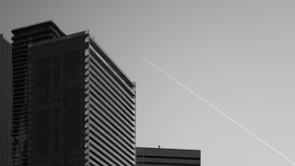 Several modern skyscrapers under a clear sky with a visible contrail diagonally spanning the background. The architecture features sleek lines and glass facades, emphasizing urban development.