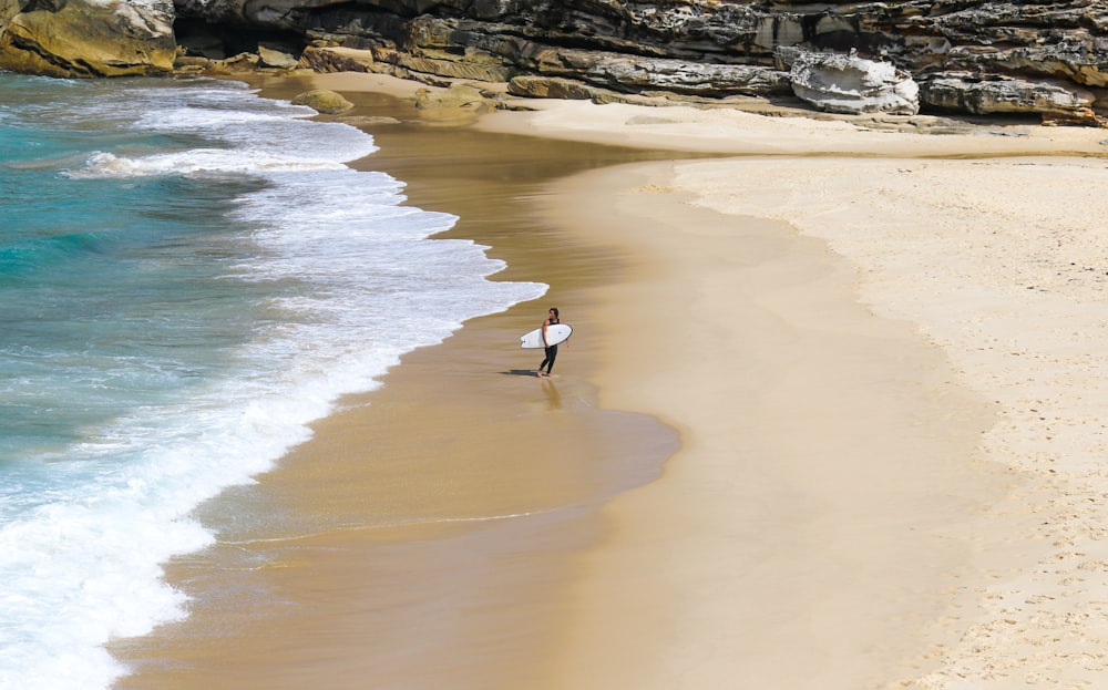 person with surf board walking beside seashore