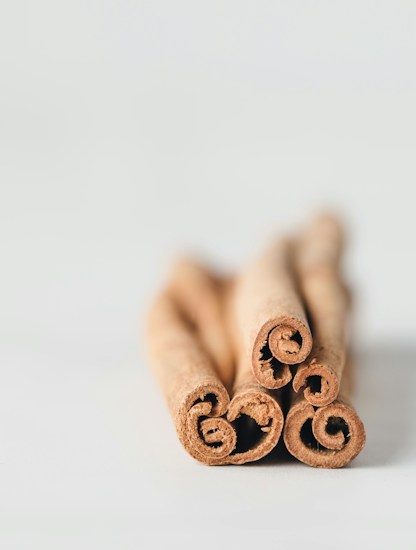 Four cinnamon sticks are arranged in a bundle, showcasing their curled ends. The image has a soft focus background, emphasizing the cinnamon&rsquo;s texture.