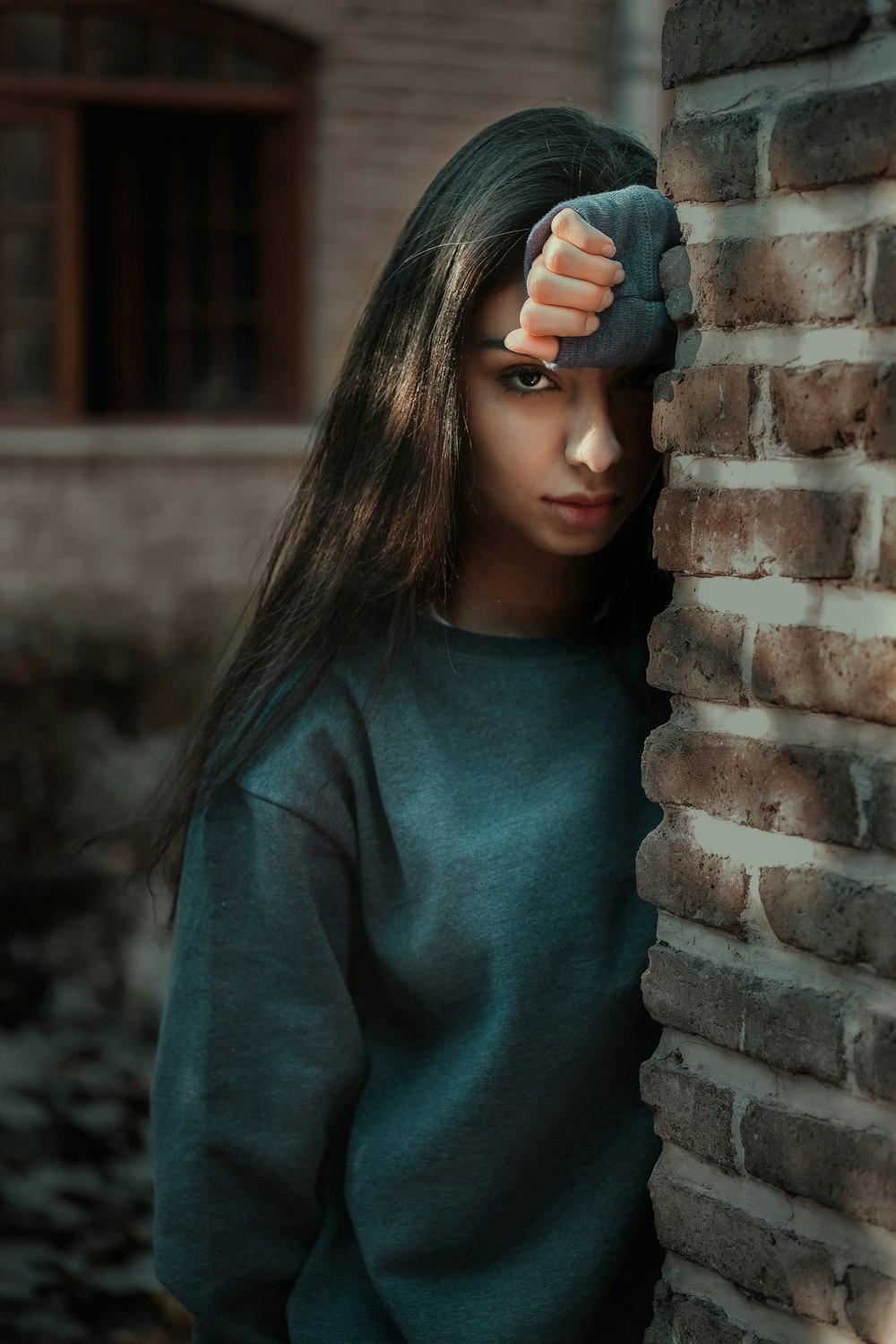 Femme en pull gris debout derrière un mur de briques brunes