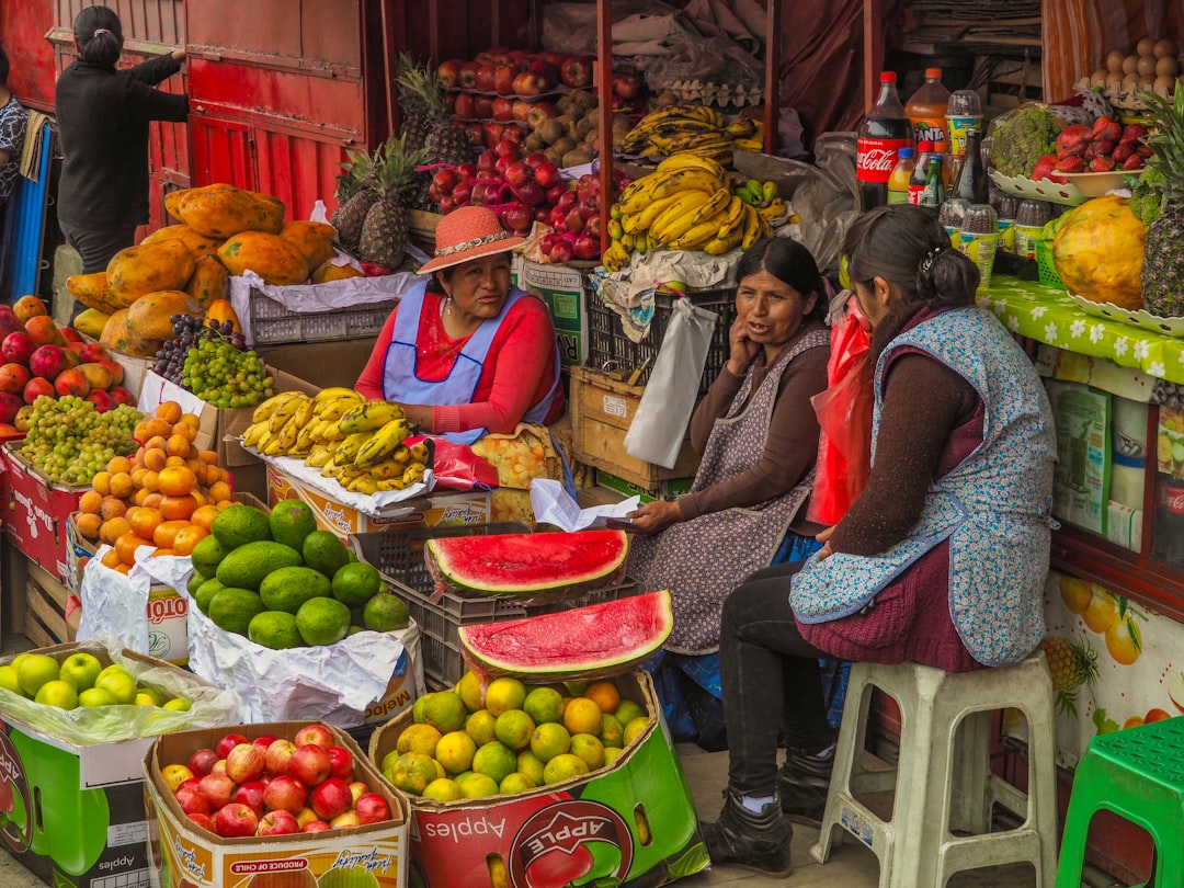 three women sitting behind assorted fruits on display in sidewalk