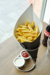 An assortment of crispy fries served in a paper cone with dipping sauces.