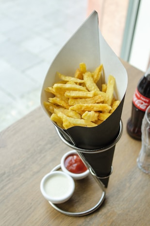 An assortment of crispy fries served in a paper cone with dipping sauces.