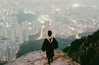 person in black top standing on cliff over looking buildings