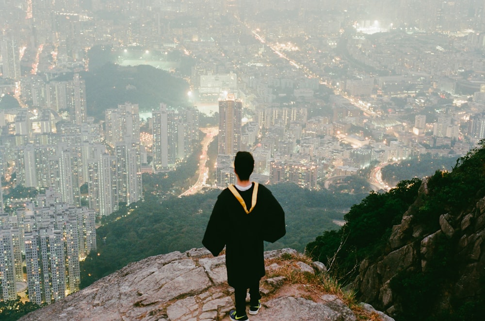 person in black top standing on cliff over looking buildings