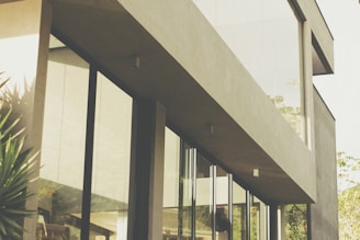 A modern architectural design showcasing a sleek building with large windows surrounded by greenery.