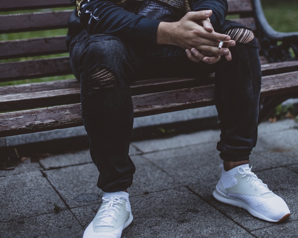 person in black distressed pants and white running shoes