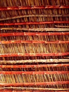 An arrangement of parallel bamboo sticks reinforced with horizontal wooden slats. The bamboo appears aged with natural imperfections, while the wood has a reddish-brown hue, creating an earthy texture.