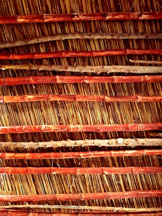 An arrangement of parallel bamboo sticks reinforced with horizontal wooden slats. The bamboo appears aged with natural imperfections, while the wood has a reddish-brown hue, creating an earthy texture.