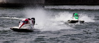 Two speedboats racing across a body of water with splashes trailing behind them. The boat on the left has a red and white color scheme, while the one on the right is primarily green. The movement creates dynamic waves on the water surface.