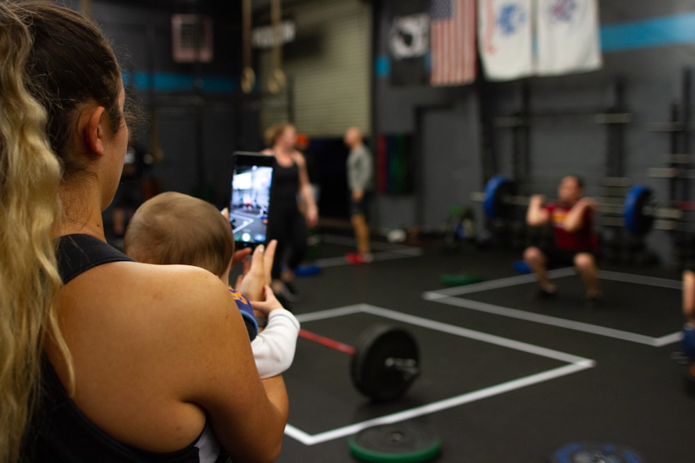 woman carrying baby while using smartphone inside gym