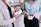 Two people are engaged in a transaction, one holding a small container with a digital payment logo and the other holding a bottle of tea. They are both dressed in casual clothing, standing inside a shop with shelves in the background displaying various products.