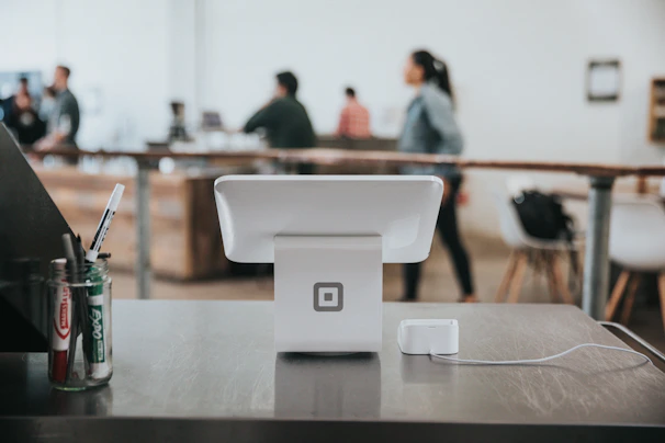Close-up of a sleek Square POS device on a wooden counter with coffee shop background.