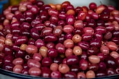 A pile of vibrant, glossy olives of varying shades of red and pink is displayed. The fruits are closely packed together, showcasing a rich, shiny surface that highlights their freshness.