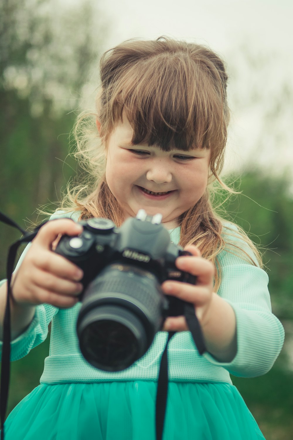 smiling girl in green dress holding Nikon DSLR camera