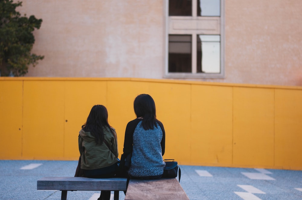 two persons sitting on brown bench