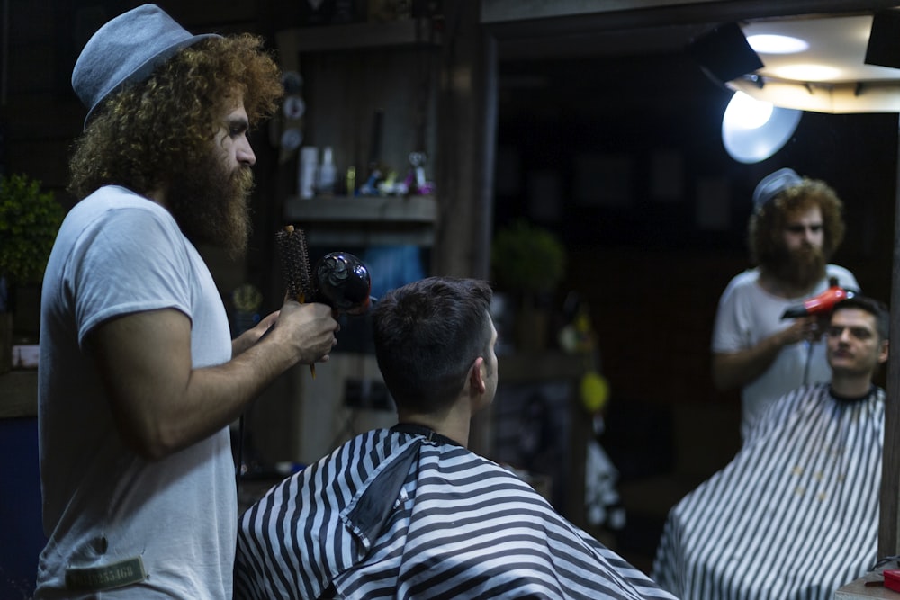 man holding blower of person sitting on barber shop