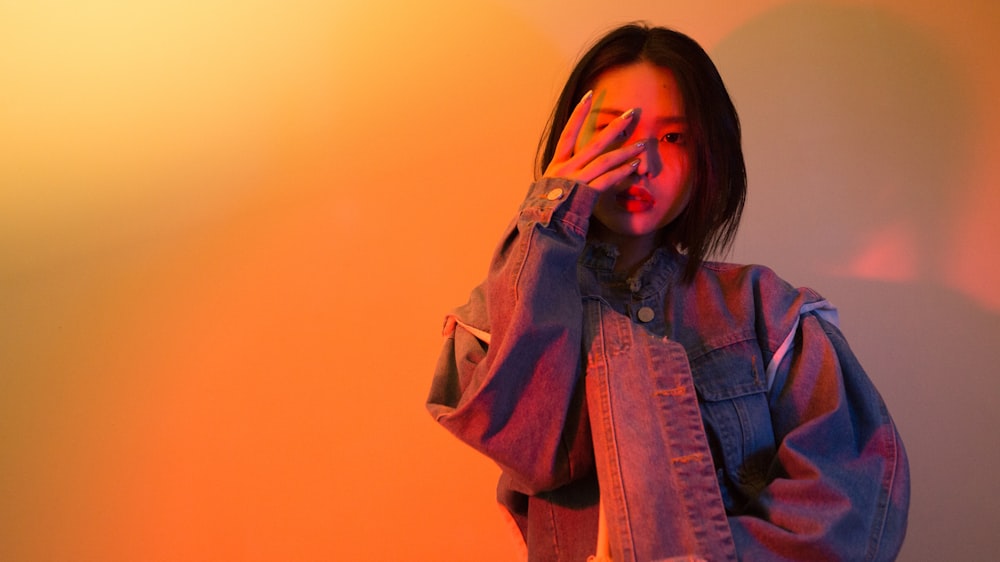 woman in denim jacket covering face with fingers