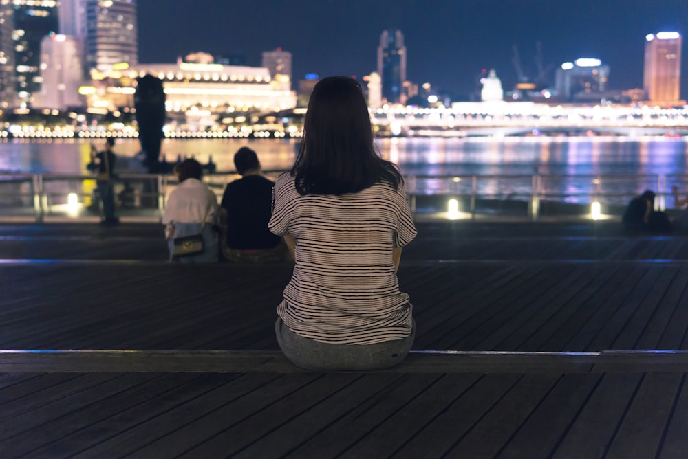 woman sitting on concrete platform facing lighted buildings