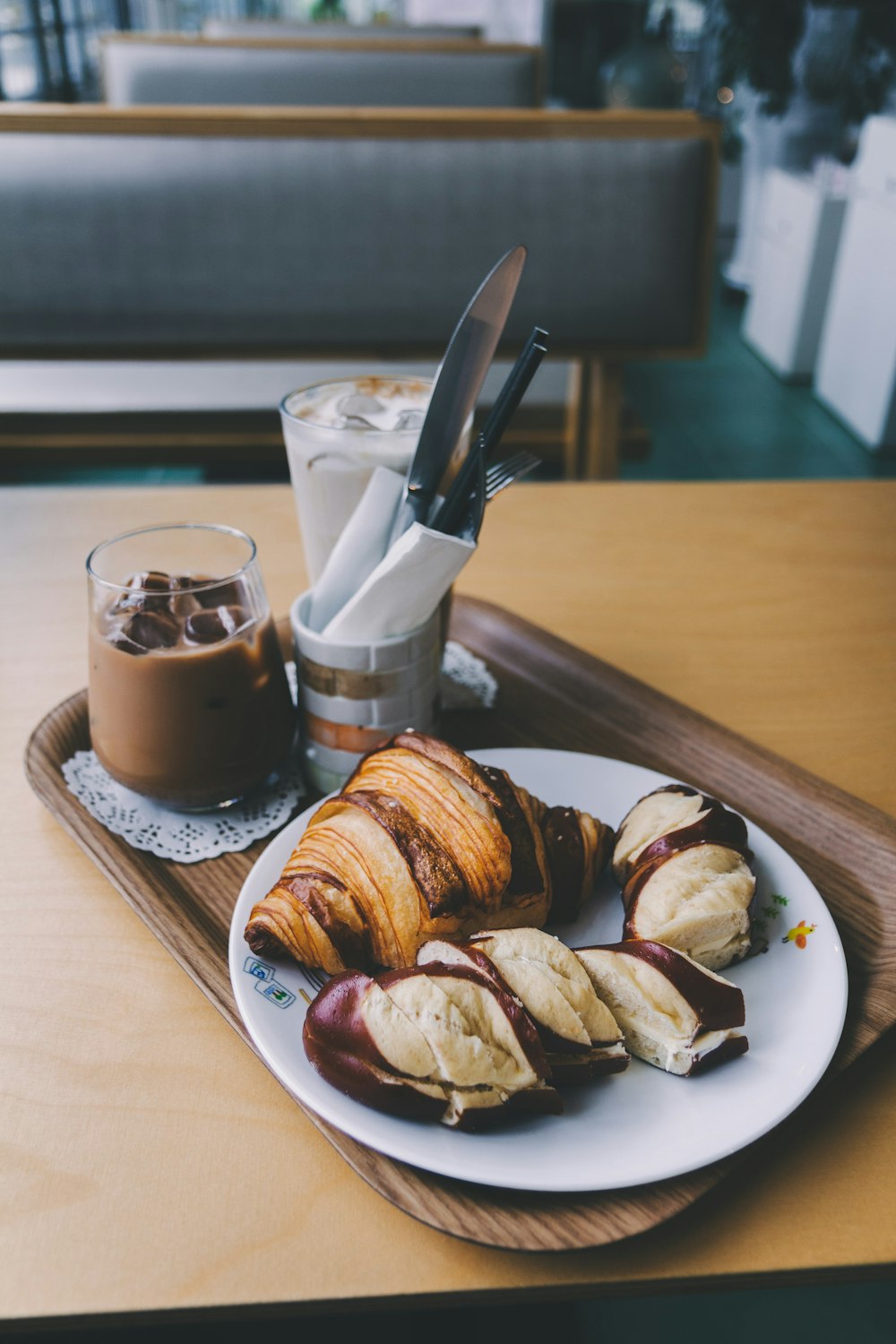 croissant on plate near ice cold drinks in cup beside gray stainless steel knife on brown tray