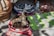 A cat is comfortably lying on a multicolored woven mat. Surrounding the cat are vibrant rugs with intricate patterns and a plastic bottle of water nearby. The setting appears relaxed with diverse textiles under a mix of sun and shadows.