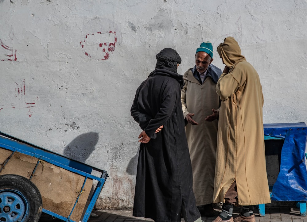 three men in thawb standing near grey concrete wall