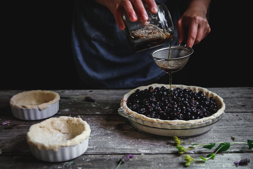 person pouring liquid on blackberry pie