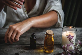 A person applying oil from a glass dropper onto their arm at a table